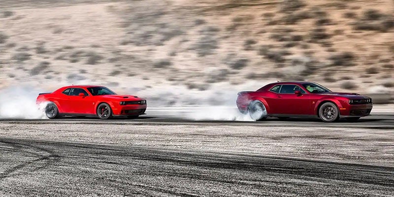 Two Dodge cars drivng quickly with smoking tires